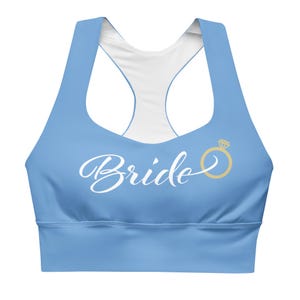 May include: A light blue sports bra with a white interior and a racerback design. The word "Bride" is written in white script across the front, with a gold ring graphic to the right.