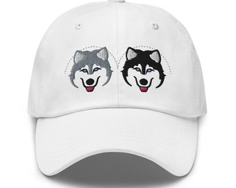May include: White baseball cap with embroidered images of two husky dogs, one gray and one black, with blue eyes and pink tongues.