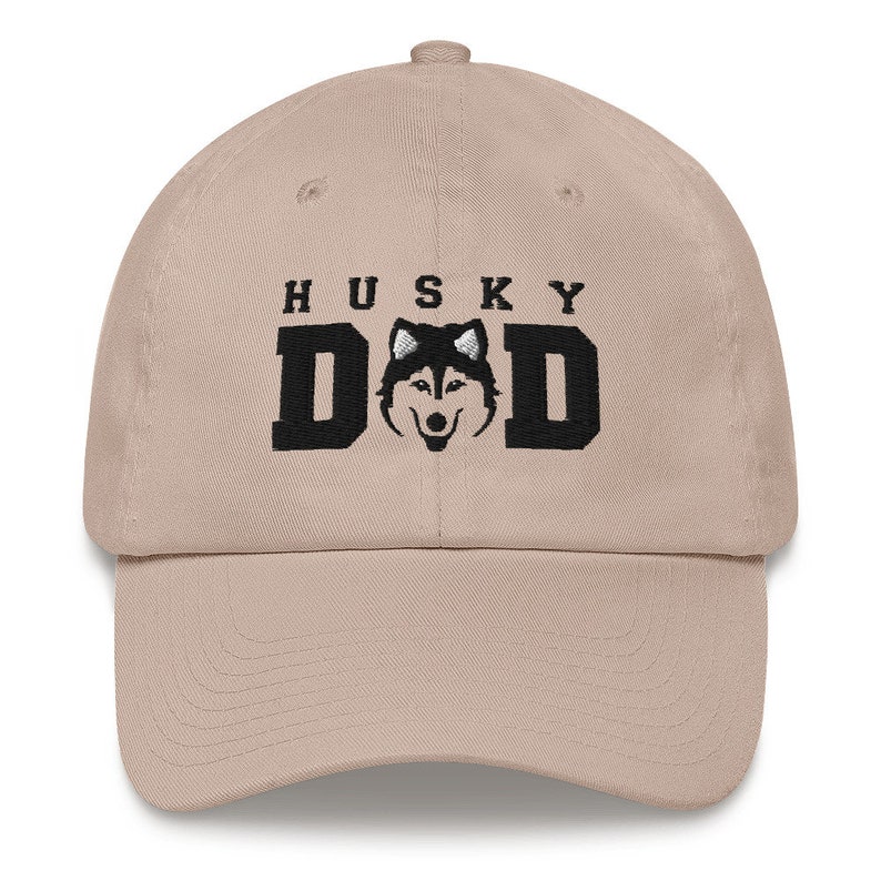 May include: Tan colored baseball cap with black embroidered text that reads "HUSKY DAD" and a black and white husky silhouette.