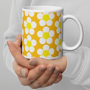 May include: White ceramic mug with a yellow background and a pattern of white daisies with yellow centers.