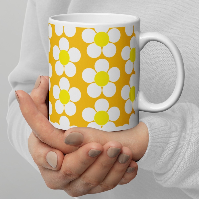 May include: White ceramic mug with a yellow background and a pattern of white daisies with yellow centers.