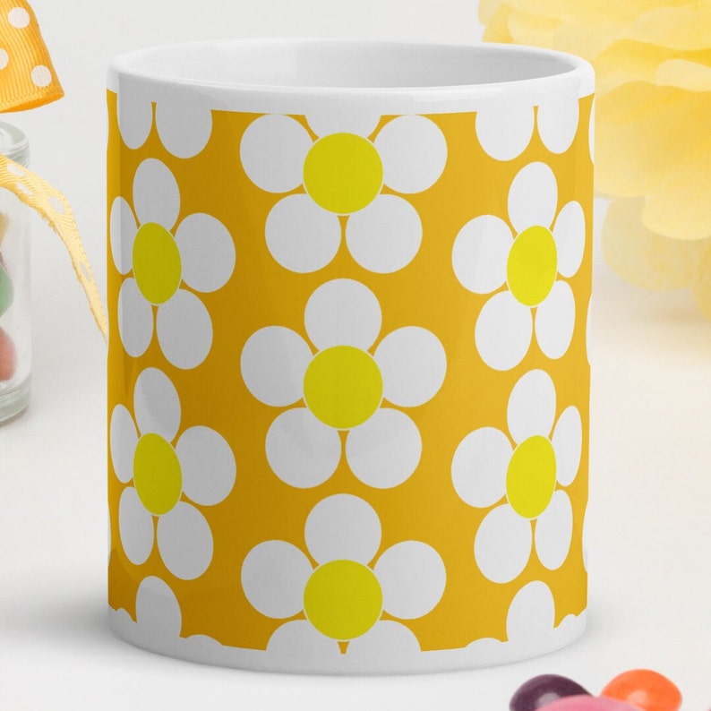 May include: A white ceramic mug with a yellow background and a repeating pattern of white daisies with yellow centers.