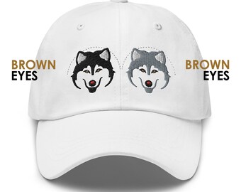 Peut inclure: Casquette de baseball blanche avec des visages de chiens husky brodés sur le devant. Le texte "BROWN EYES" est brodé de chaque côté des visages de chiens.