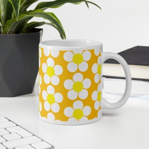 May include: White ceramic mug with a yellow background and a pattern of white daisies with yellow centers.