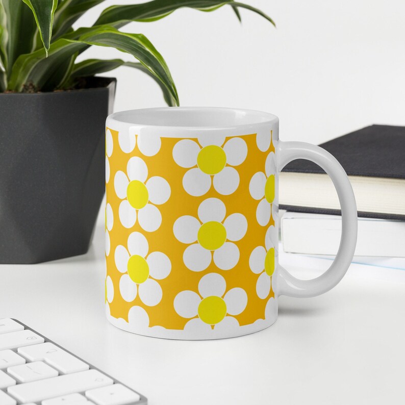 May include: White ceramic mug with a yellow background and a pattern of white daisies with yellow centers.