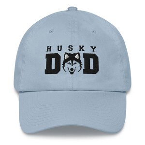 May include: A light blue baseball cap with black embroidery that reads "HUSKY DAD" and features a black and white husky silhouette.