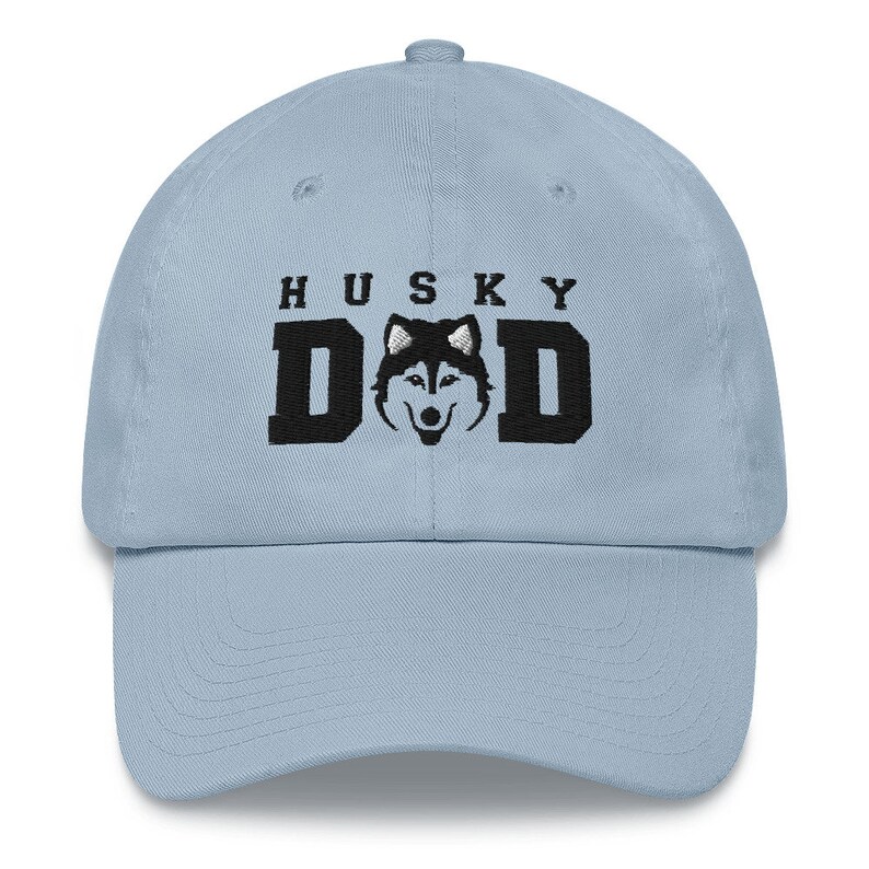 May include: A light blue baseball cap with black embroidery that reads "HUSKY DAD" and features a black and white husky silhouette.