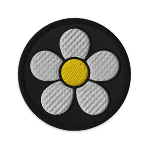 Könnte beinhalten: Gestickter Aufnäher mit einem Gänseblümchen-Design. Der Aufnäher hat einen schwarzen kreisförmigen Hintergrund mit einem schwarz genähten Rand. Das Gänseblümchen hat fünf weiße Blütenblätter und eine gelbe Mitte.