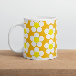 May include: White ceramic mug with a yellow and white daisy pattern. The daisies are stylized and have a yellow center.
