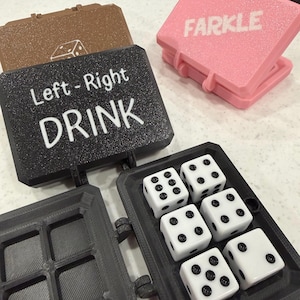 May include: A collection of dice games, including a black case with "Left-Right DRINK" text, a pink case with "FARKLE" text, and a brown case with a die symbol. Six white dice with black dots are in a gray case.