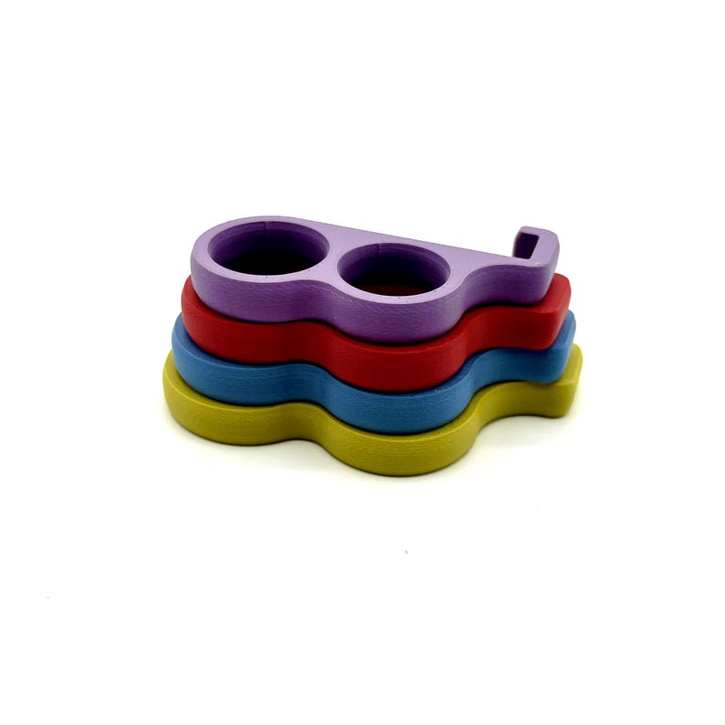 May include: A stack of four colorful, wooden coasters. The top coaster is purple with two circular cutouts. Below it are red, blue, and yellow coasters, each with a unique, wavy shape. The coasters are designed to protect surfaces from drink rings.