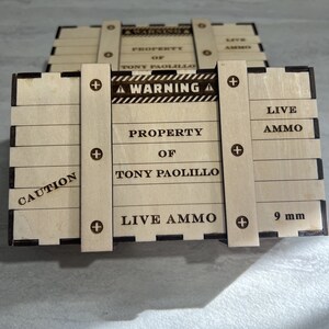 May include: A wooden box with a warning sign that reads "WARNING" and "LIVE AMMO". The box is labelled "PROPERTY OF TONY PAOLILLO" and "CAUTION". The box is also labelled "9 mm".