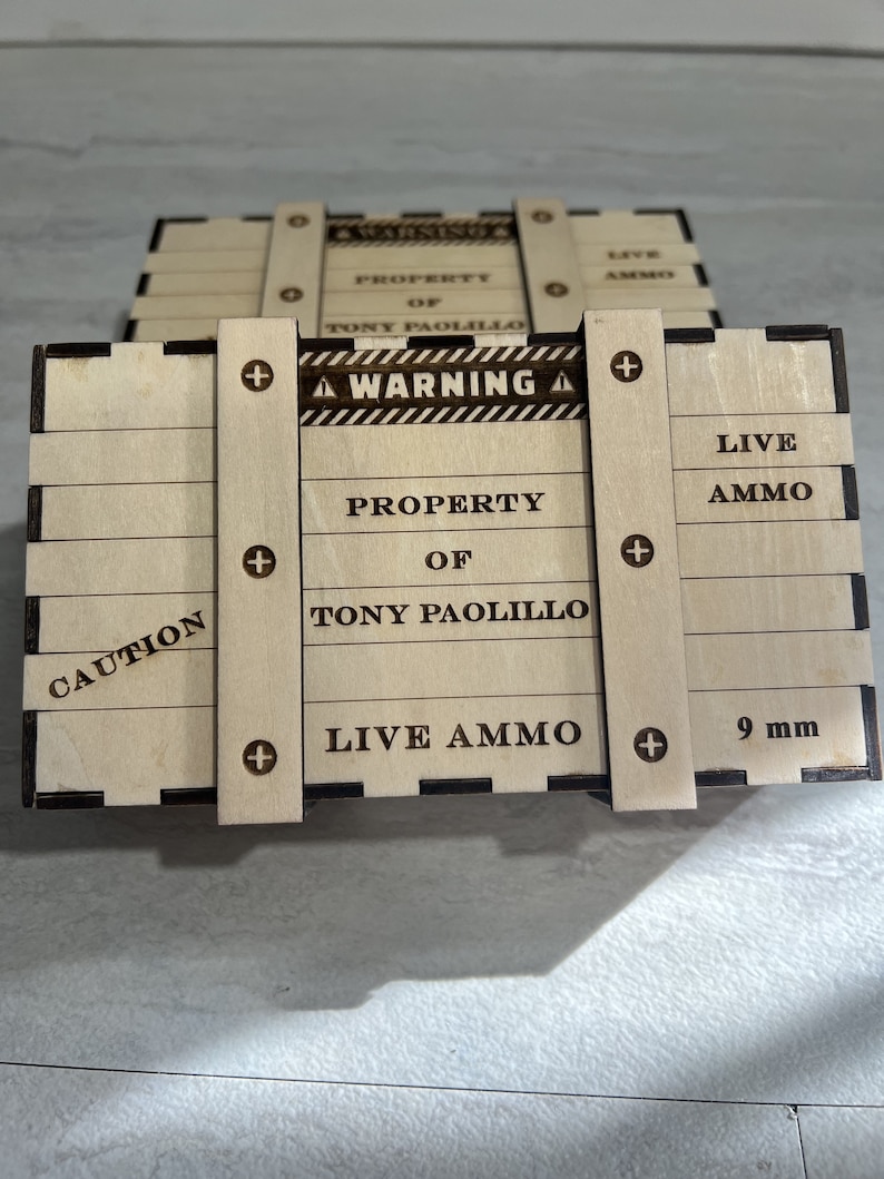 May include: A wooden box with a warning sign that reads "WARNING" and "LIVE AMMO". The box is labelled "PROPERTY OF TONY PAOLILLO" and "CAUTION". The box is also labelled "9 mm".
