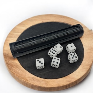 May include: A black dice shaker and six white dice with black dots are arranged on a wooden and black surface. The dice shaker is a long, cylindrical shape. The dice show different numbers from one to six.