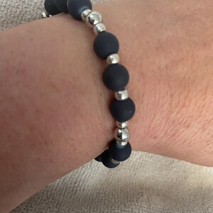 May include: A dark blue beaded bracelet with silver-colored metal accents. The bracelet features matte, round beads interspersed with smaller, shiny metal beads. The bracelet is worn on a wrist.