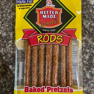 May include: A yellow bag of Better Made Special Rods baked pretzels. The bag features a red and yellow logo with the text "Better Made Special" and "Since 1930". The bag also features the text "RODS" in large red letters and "Baked Pretzels" in black letters. The bag contains several pretzel rods.