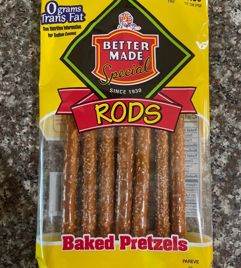 May include: A yellow bag of Better Made Special Rods baked pretzels. The bag features a red and yellow logo with the text "Better Made Special" and "Since 1930". The bag also features the text "RODS" in large red letters and "Baked Pretzels" in black letters. The bag contains several pretzel rods.