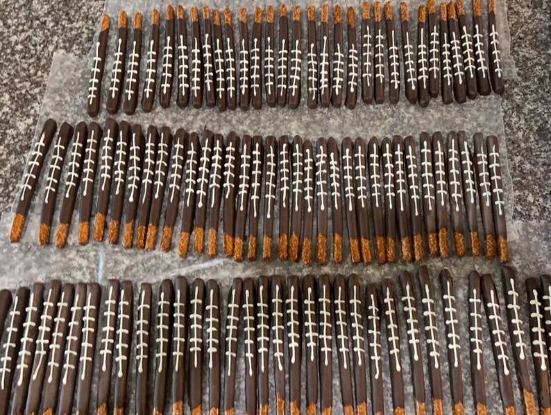 May include: A large quantity of chocolate-covered pretzel sticks decorated with white icing to resemble footballs.
