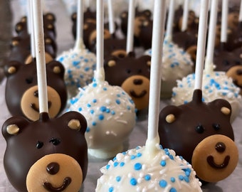 May include: A close-up of a table with a variety of cake pops. The cake pops are decorated with chocolate and white frosting, and some have blue sprinkles. The cake pops are on sticks and are arranged in a row.