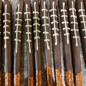 May include: A dozen chocolate-covered pretzel rods with white icing designs resembling football stitches.