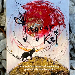 Puede incluir: Una baraja de cartas titulada "Jaguar Kel" con un diseño abstracto rojo y dorado. La portada presenta una silueta de jaguar negro, una mariposa y el texto "a sacred Oracle Deck of awakening guided by the earth and sky."