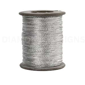 May include: A spool of metallic silver thread wound tightly around a dark brown cylindrical core. The thread has a reflective, shimmering texture and is wrapped in uniform horizontal layers from the top to the bottom of the spool.