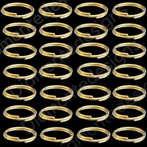 以下が含まれることがあります： 30個の金色のキーリングのセット。キーリングはすべて同じサイズと形であり、グリッドパターンで配置されています。