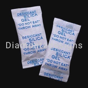 Könnte beinhalten: Zwei rechteckige weiße Trockenmittelbeutel aus Kieselgel mit blauem Aufdruck, der DESICCANT SILICA GEL DO NOT EAT THROW AWAY lautet. Die Beutel haben eine texturierte, papierartige Oberfläche mit versiegelten Kanten an der Ober- und Unterseite.