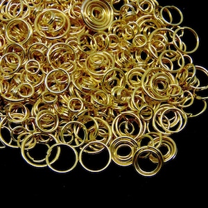 May include: A large pile of gold-coloured metal jump rings. The rings are of various sizes and are arranged in a random pattern.