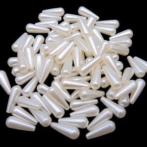 May include: A large pile of white teardrop-shaped beads. The beads are made of plastic and have a pearlescent finish.