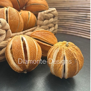 Könnte beinhalten: Eine Sammlung getrockneter Orangen-Pomander mit texturierter, gold-orangener Schale und vertikalen Schlitzen, teilweise in einem geflochtenen Korb. Der Text Diamonte-Designs ist in Weiß über die Bildmitte gelegt.