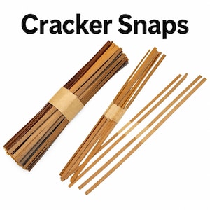 May include: A collection of Cracker Snaps consisting of thin, flat, brown wooden strips. One large bundle is secured with a tan paper band, while a smaller group is partially fanned out and held by a similar band, with two loose strips lying nearby.