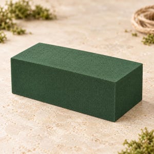 May include: A rectangular block of dark green floral foam with a porous, textured surface. The object is a solid, uniform shape designed for arranging flowers, featuring sharp edges and a consistent matte finish across all visible sides.