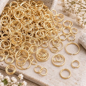 May include: A large collection of gold-toned metal jump rings in various sizes. These circular jewellery findings feature a smooth, polished finish and a small opening on each ring, allowing them to be easily connected for crafting jewellery pieces.
