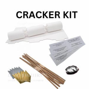 Puede incluir: Un kit de petardos blanco con el texto "CRACKER KIT". El kit incluye petardos de papel blanco, tiras de papel marrón, pequeños trozos de papel plateado y dorado, y pequeñas tarjetas blancas con texto impreso.