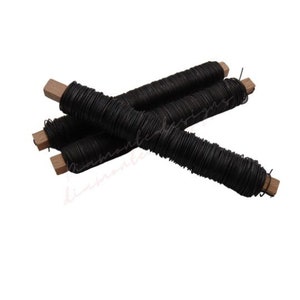 Puede incluir: Tres carretes de alambre floral negro envueltos alrededor de clavijas de madera.