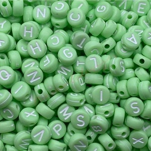 May include: A close-up of a large pile of light green round beads with white letters on them. The letters are all different and include A, B, C, D, E, F, G, H, I, J, K, L, M, N, O, P, Q, R, S, T, U, V, W, X, Y, and Z.