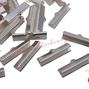 May include: A close-up of a pile of silver metal clasps for ribbon or fabric. The clasps are about 1 inch long and have a textured surface.