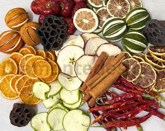 May include: A collection of dried botanical elements including orange slices, apple slices, lime slices, whole red chili peppers, cinnamon sticks, dark brown lotus seed pods, and small round red fruits arranged on a light surface.