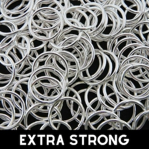 Op de afbeelding: Een grote stapel zilveren springringen. De ringen zijn allemaal even groot en zijn in een willekeurig patroon gerangschikt. De tekst "EXTRA STRONG" is onderaan de afbeelding gedrukt.