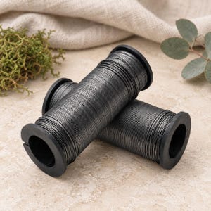 May include: Two cylindrical spools of thin, dark charcoal-coloured metal wire. Each spool features a black plastic core with circular end caps, holding a tightly wound coil of wire that spans the length of the central cylinder between the caps.