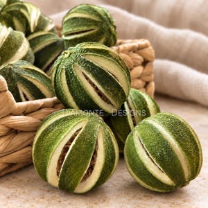 May include: A collection of dried, spherical green limes with deep vertical slits revealing a textured, light brown interior. The limes are arranged in and around a woven basket, with the text DIAMONTE DESIGNS overlaid in white lettering.