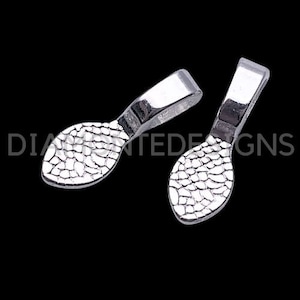Puede incluir: Dos baúles de colgante de metal plateado con un diseño texturizado y estampado. Los baúles tienen forma de lágrima alargada.