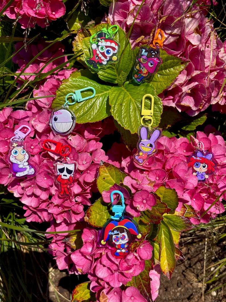 May include: A collection of colorful acrylic keychains featuring various cartoon characters. The keychains have different shapes and designs, including a jester, a bunny, and other whimsical figures. Each keychain has a metal clasp for attachment.