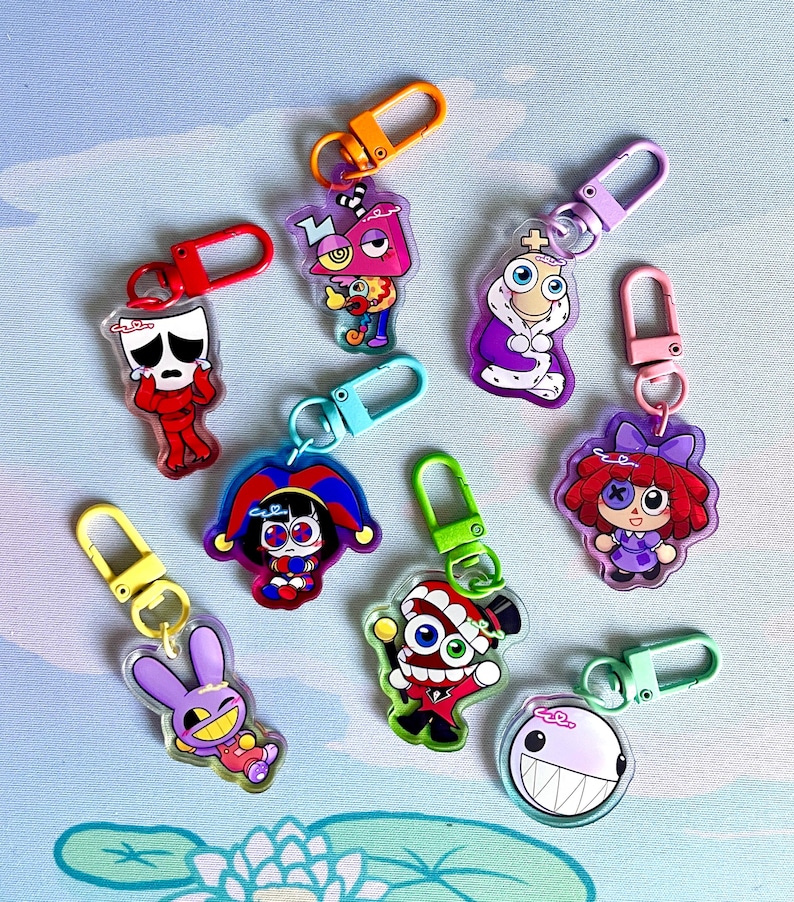 May include: A collection of acrylic keychains featuring colorful cartoon characters with various designs. Each keychain has a different character with unique features, attached to a metal clasp in various colors like red, orange, and green.