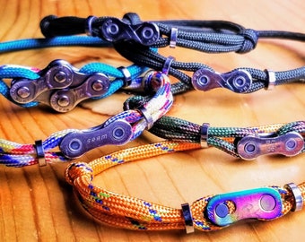 May include: Five colourful bracelets with metal bike chain links. The bracelets are made of different coloured paracord and feature a variety of chain link styles.