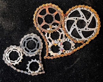 Puede incluir: Dos corazones de metal hechos de cadena de bicicleta y engranajes. Los corazones están oxidados y tienen un aspecto vintage.