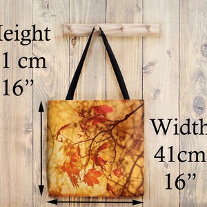 May include: A tote bag with a fall-themed design featuring a branch of red maple leaves against a backdrop of golden light. The bag measures 16 inches in height and 16 inches in width.