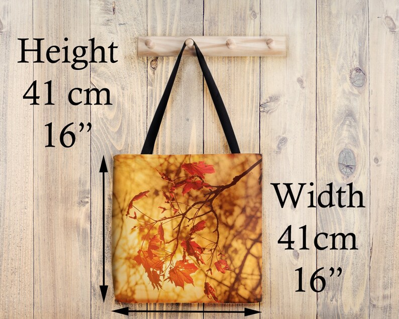 May include: A tote bag with a fall-themed design featuring a branch of red maple leaves against a backdrop of golden light. The bag measures 16 inches in height and 16 inches in width.