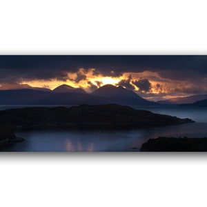 Könnte beinhalten: Ein Panoramablick auf eine Bergkette, die sich vor einem dramatischen Sonnenuntergangshimmel abzeichnet. Der Himmel ist gefüllt mit leuchtenden orangefarbenen und gelben Wolken, während die Berge dunkel und imposant sind. Die Szene wird aus einer niedrigen Perspektive aufgenommen, was dem Betrachter ein Gefühl von Größe und Erhabenheit vermittelt.